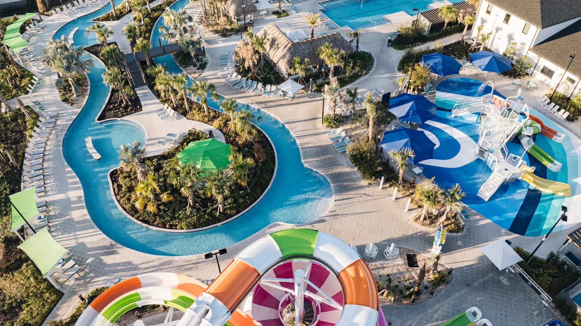 High-angle aerial view of a resort water park featuring a large multi-lane slide tower, a winding lazy river, and a children's splash pad with a dump bucket.