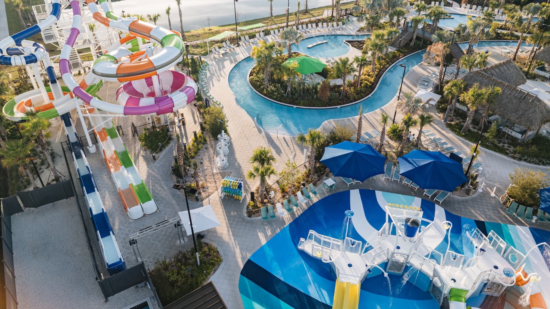 High-angle aerial view of a resort water park featuring a large multi-lane slide tower, a winding lazy river, and a children's splash pad with a dump bucket.